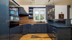 A modern kitchen with dark cabinetry, a wooden floor, and a large window. - Apartments Alin (Dramalj)