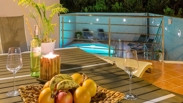 A table with a fruit basket, two wine glasses, and a candle. In the background, there is a pool area with lounge chairs. - Apartments Alin (Dramalj)