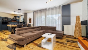 A modern living room with a sectional sofa, a white coffee table, and a kitchen in the background. - Apartments Alin (Dramalj)