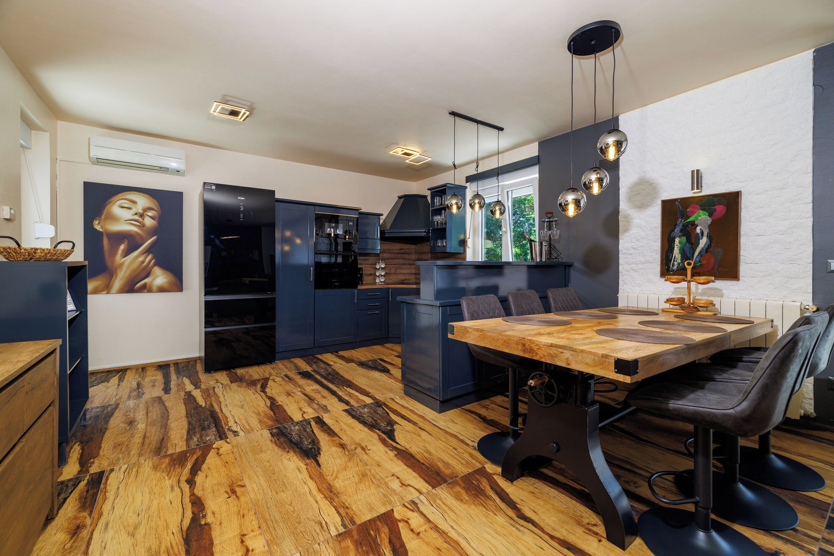 A modern kitchen with dark cabinetry, a wooden dining table, and pendant lighting.