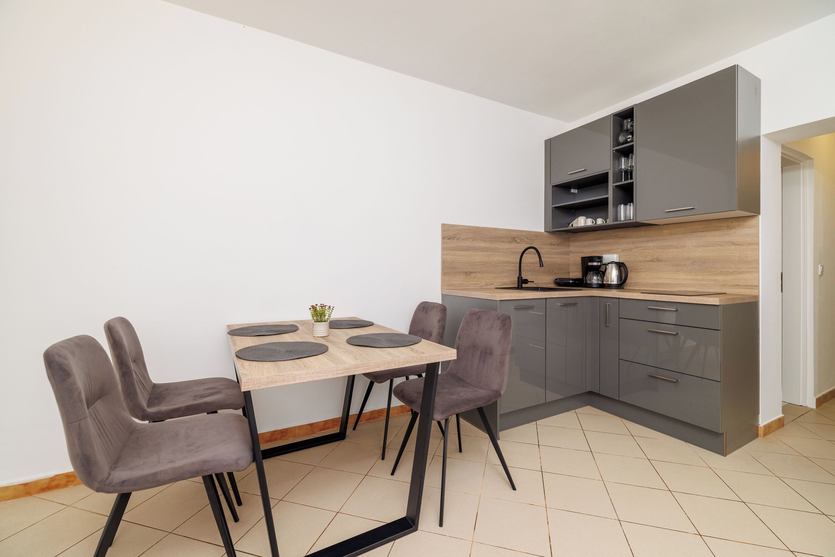 Una cocina moderna con gabinetes grises, encimera de madera y una zona de comedor con dos sillas grises y una mesa.