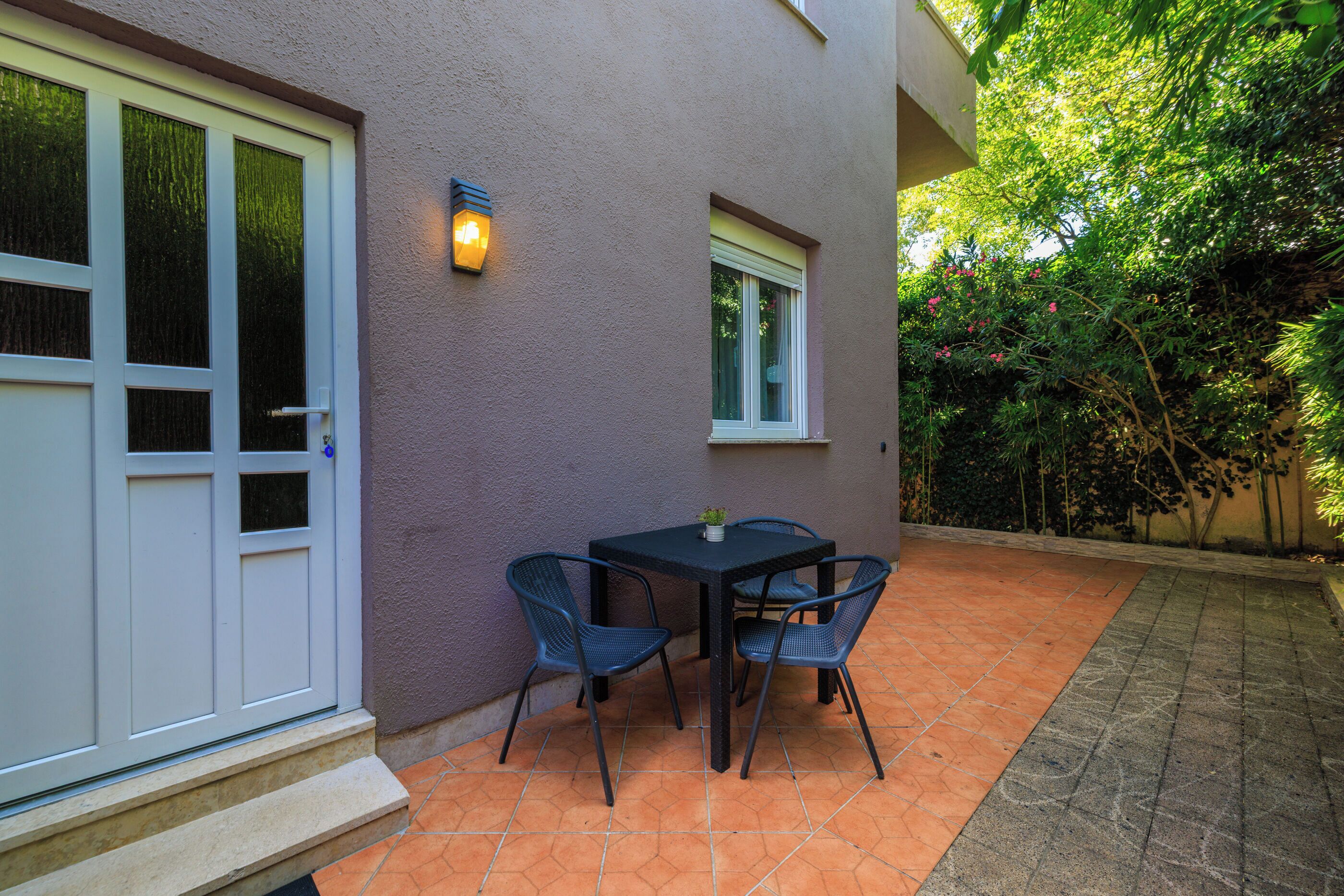 An outdoor patio with a table and chairs, a small window, and a door.