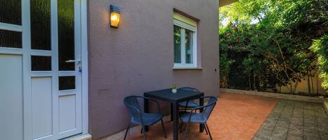 An outdoor patio with a table and chairs, a small window, and a door.