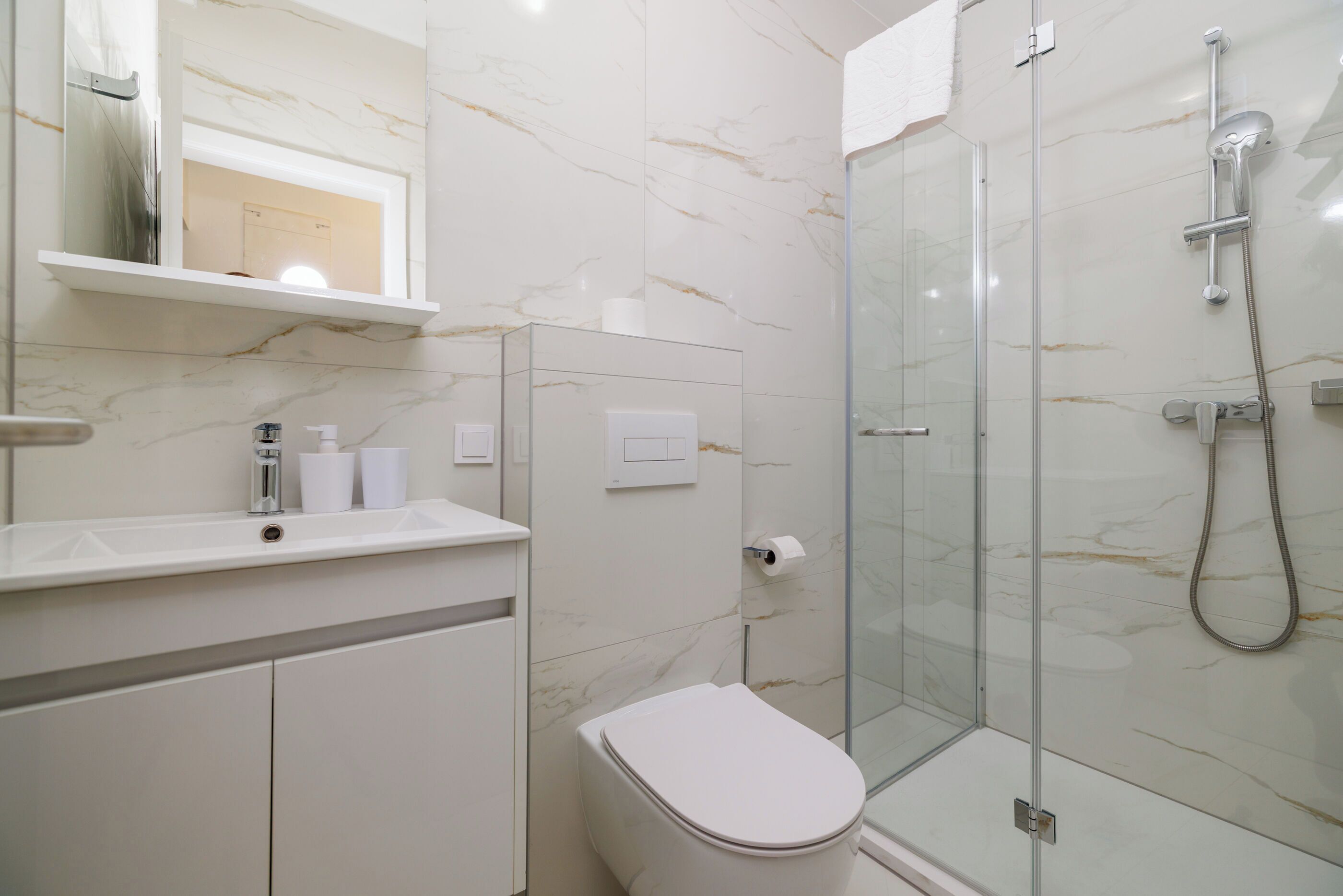 A modern bathroom with a glass-enclosed shower, a toilet, and a vanity with a mirror and sink.