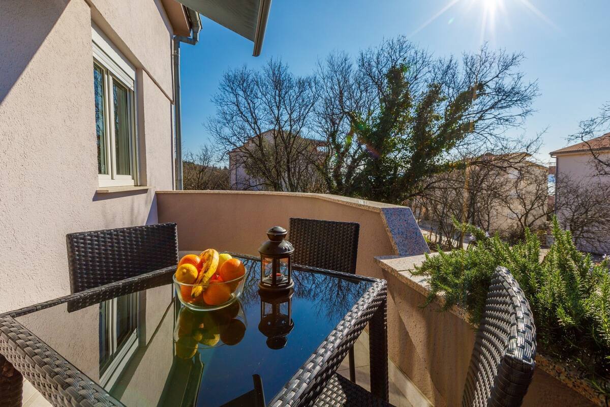 A glass-top table with wicker chairs, a bowl of fruit, and a lantern on a balcony.