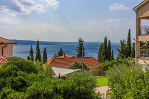 A coastal property with a red-tiled roof, a view of the sea, and surrounding greenery. - Apartments Bartulin (Crikvenica)