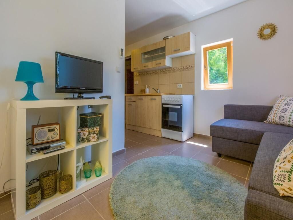 Uma sala de estar com televisão, um sofá e uma cozinha ao fundo.