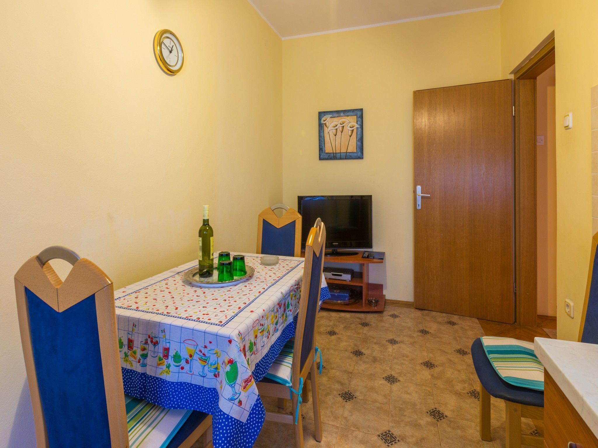 Un'area pranzo con un tavolo apparecchiato per due, una televisione e una porta in legno.