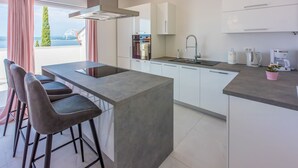 A modern kitchen with a central island, bar stools, a stainless steel range hood, a built-in oven, a sink, and a coffee machine. - Apartments Cvetkovic (Crikvenica)