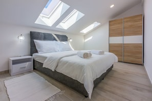 A modern bedroom with skylights, a bed with white linens, a nightstand, and a wooden wardrobe. - Apartments Cvetkovic (Crikvenica)