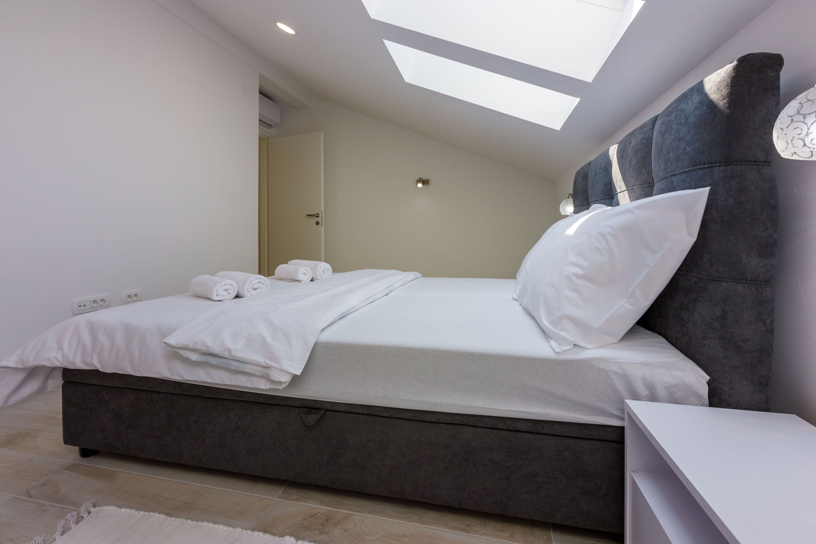 Un dormitorio moderno con una cama grande, tragaluz y cabecera gris.