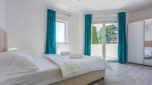 A modern bedroom with a large bed, a view of the outdoors, and a sliding door leading to a balcony. - Apartments Cvetkovic (Crikvenica)