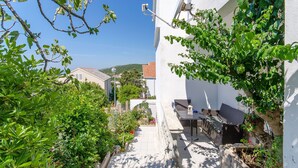 A narrow outdoor corridor with a small table and chairs, surrounded by lush greenery and a white building. - Apartment Ljubica (Zavalatica)