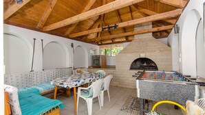 A cozy indoor space with a wooden ceiling, a foosball table, a brick fireplace, and a dining area with a table and chairs. - Apartment Ljubica (Zavalatica)