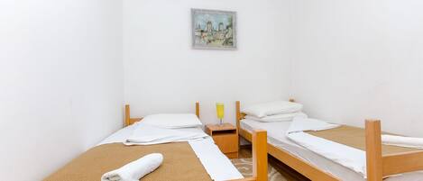 A room with two wooden beds, white bedding, a small bedside table with a glass of juice, and a painting on the wall.