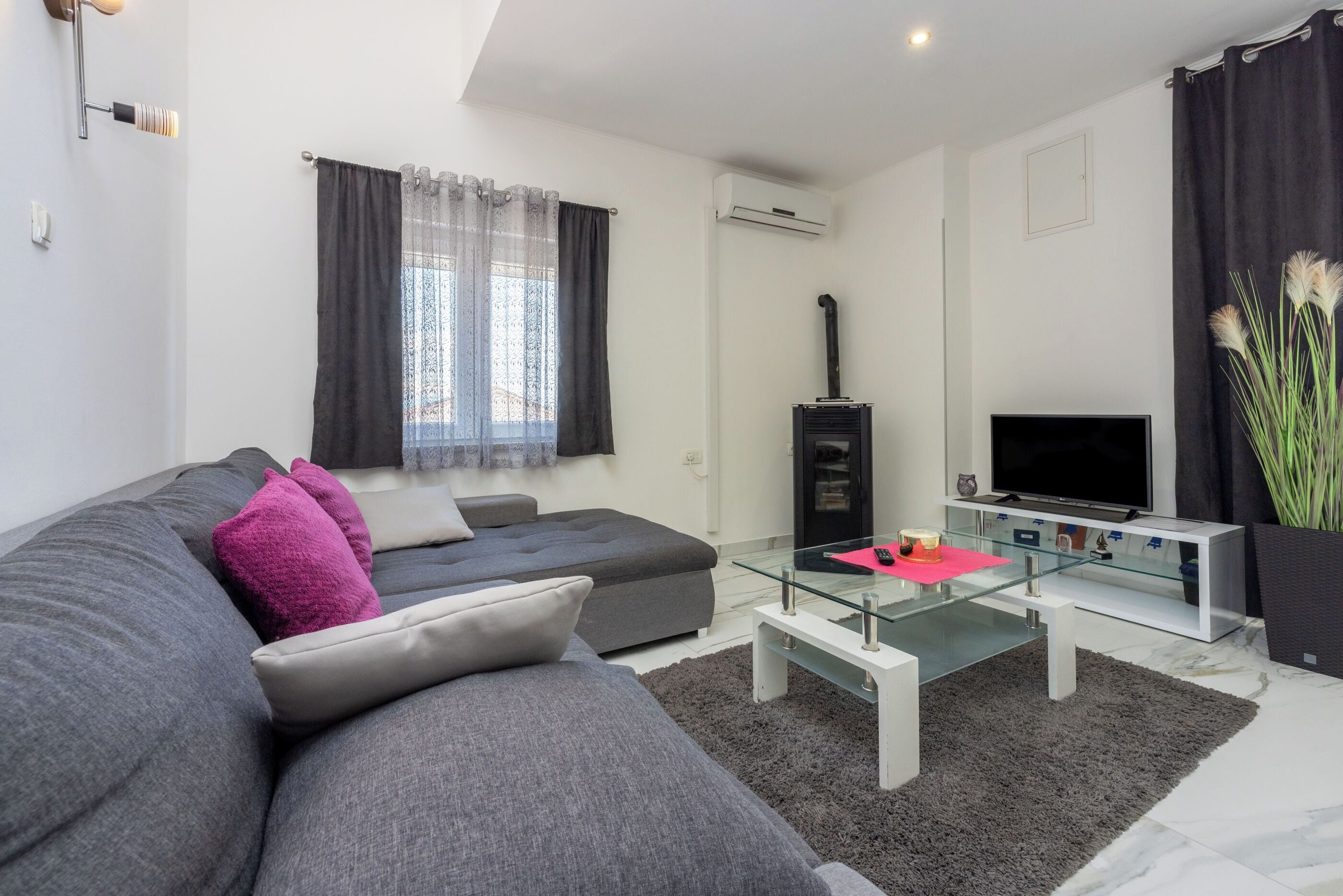 Ein modernes Wohnzimmer mit grauem Sofa, einem Glastisch, einem Flachbildfernseher und einer schwarzen Unterhaltungsanlage.