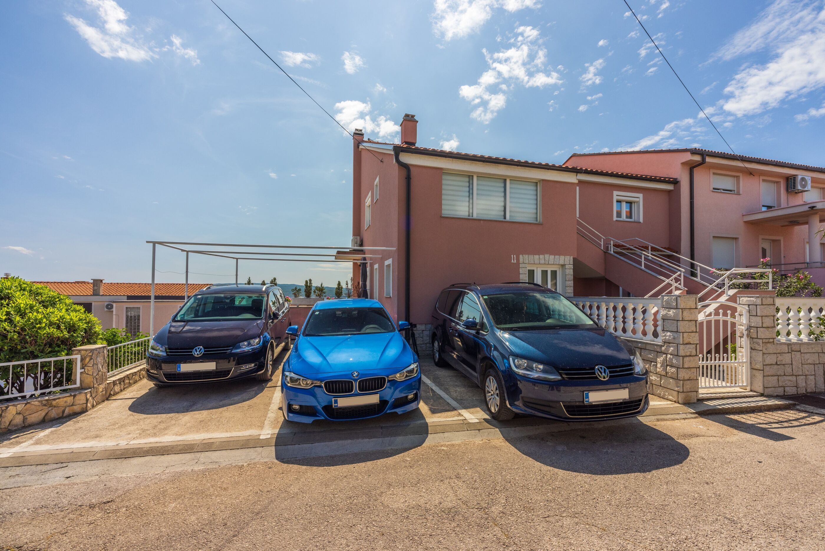 Três carros estacionados em uma entrada de garagem em frente a um edifício com telhado vermelho e paredes brancas.