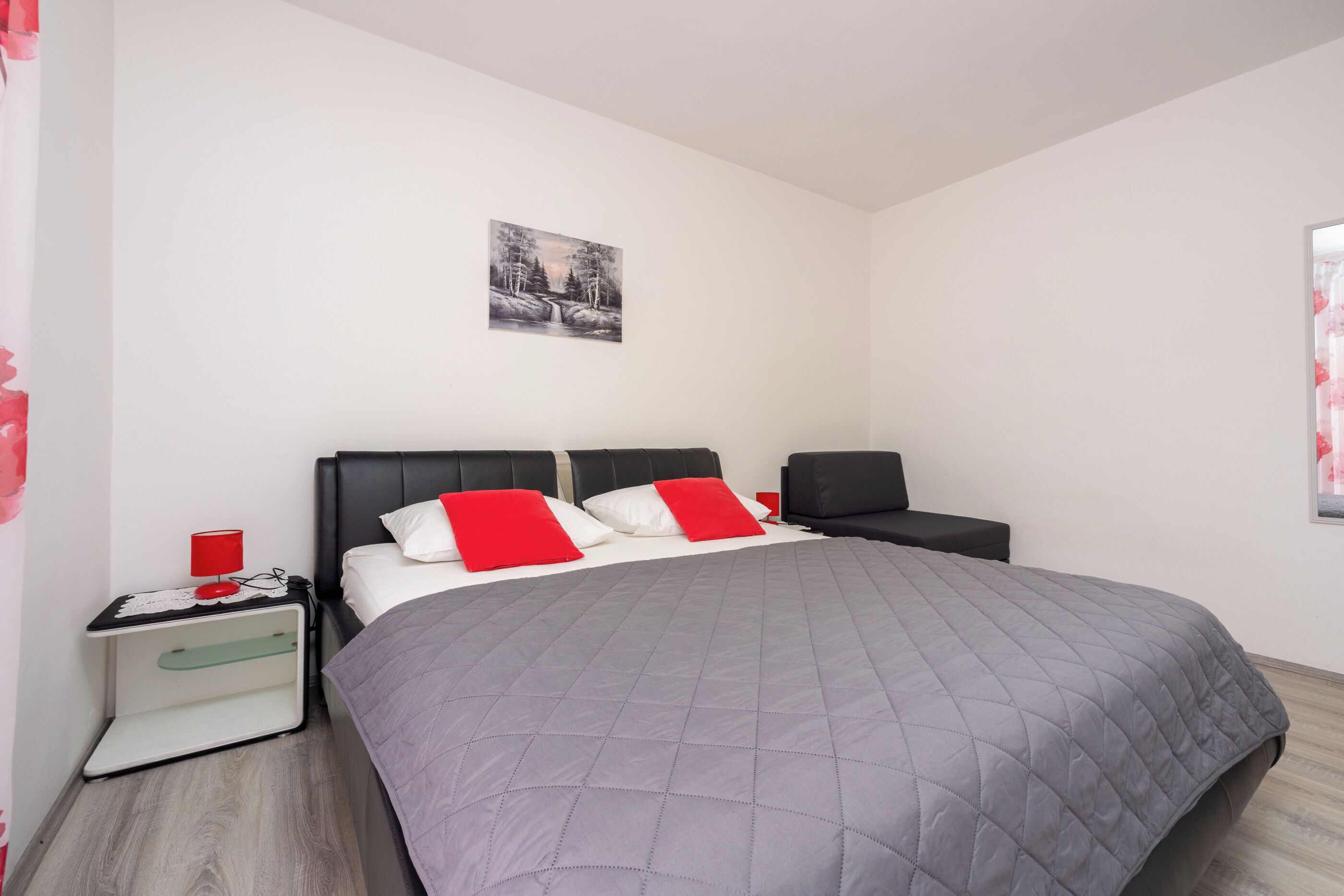 Ein modernes Schlafzimmer mit einem großen Bett, einem Nachttisch, einem Sessel und einem Bild an der Wand.
