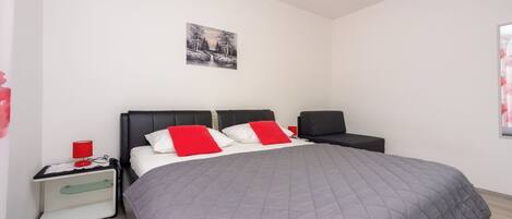 Ein modernes Schlafzimmer mit einem großen Bett, einem Nachttisch, einem Sessel und einem Bild an der Wand.