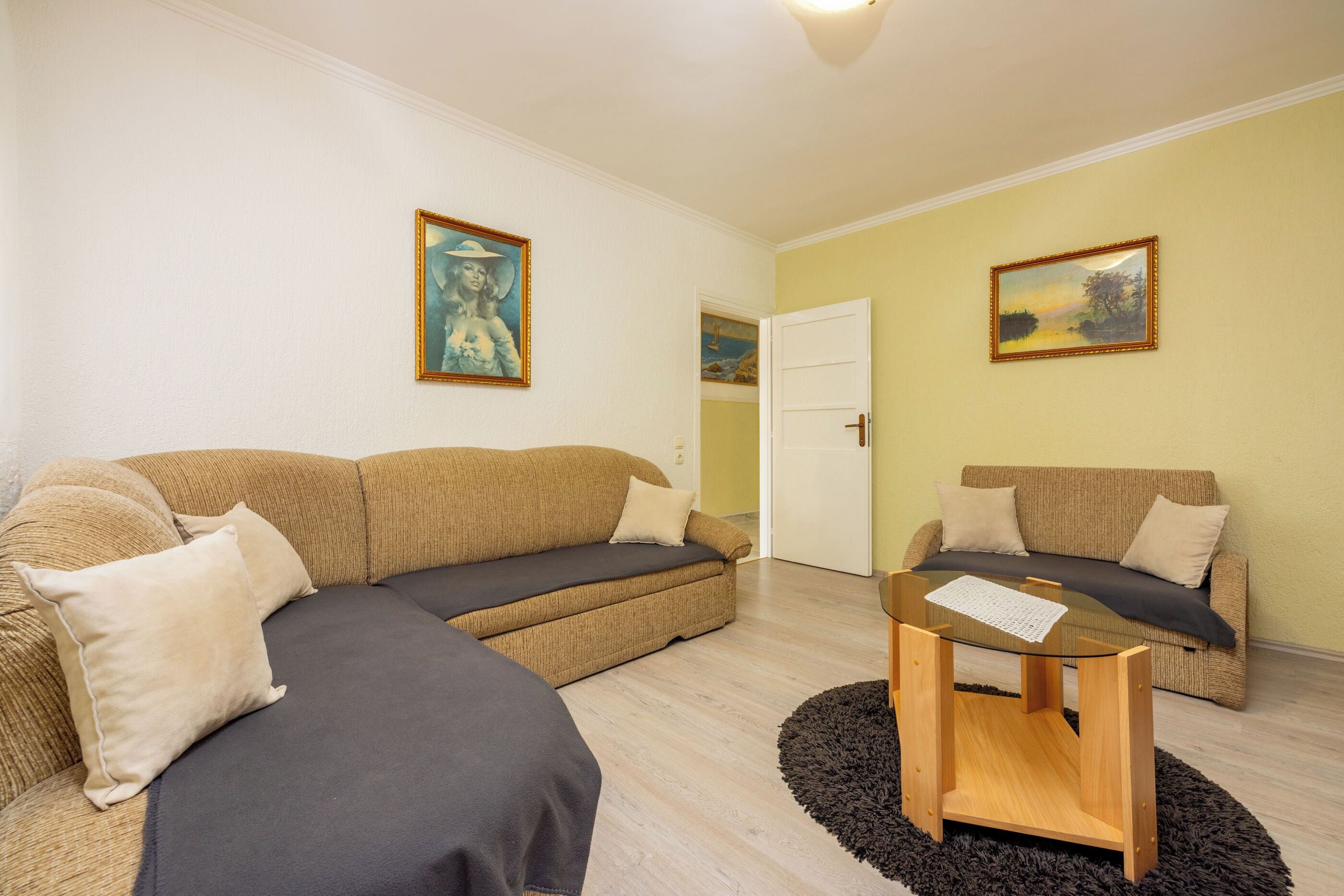 A living room with two sofas, a glass coffee table, and two paintings on the walls.