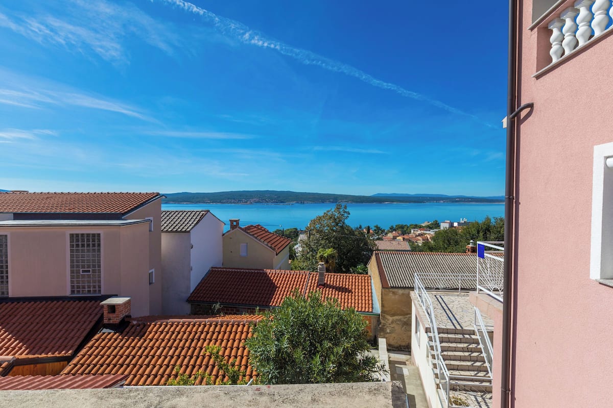 A coastal town with terracotta-tiled rooftops, a clear blue sky, and a view of the sea.