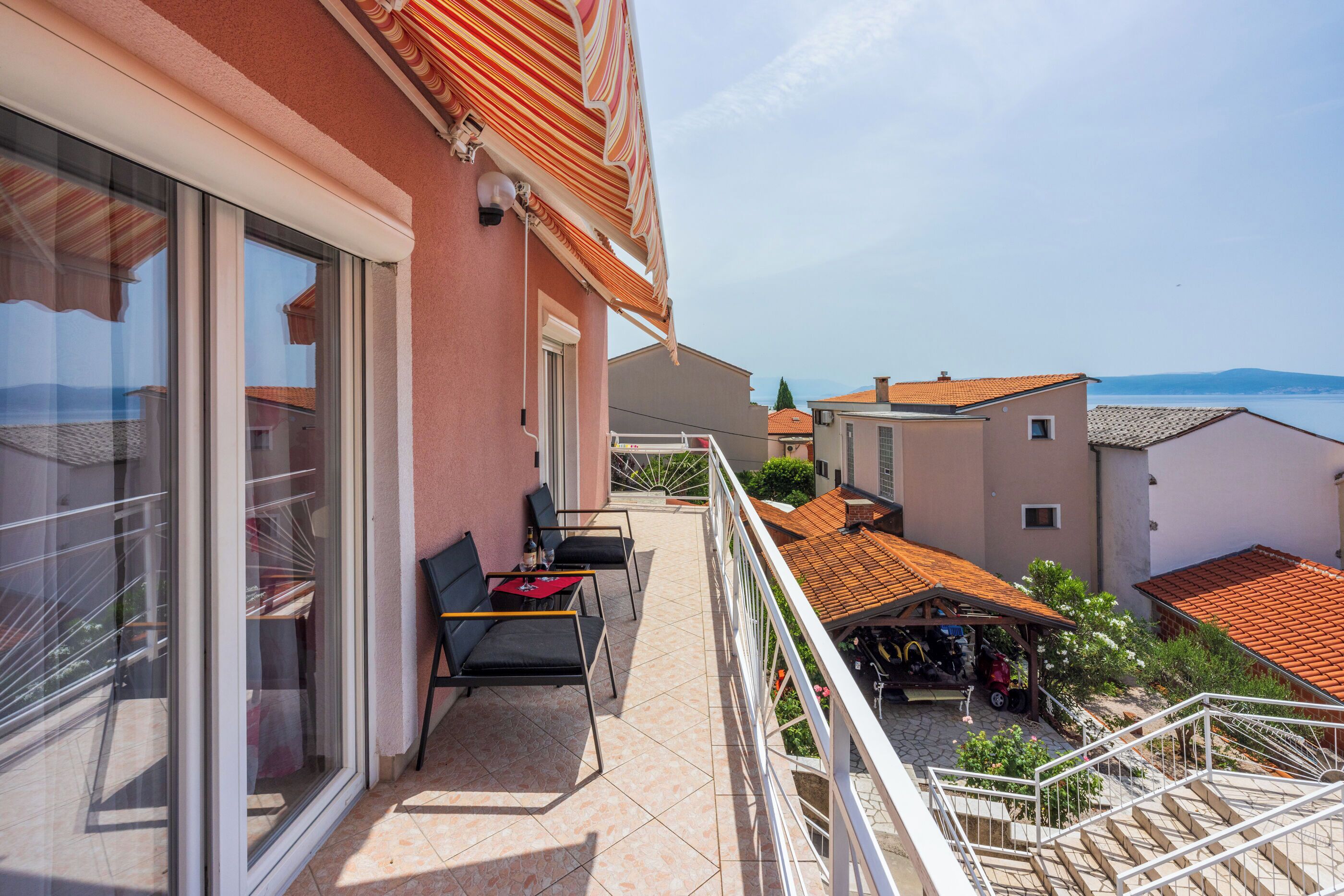 A balcony with a table and chairs, a view of the sea, and a staircase leading to another level.