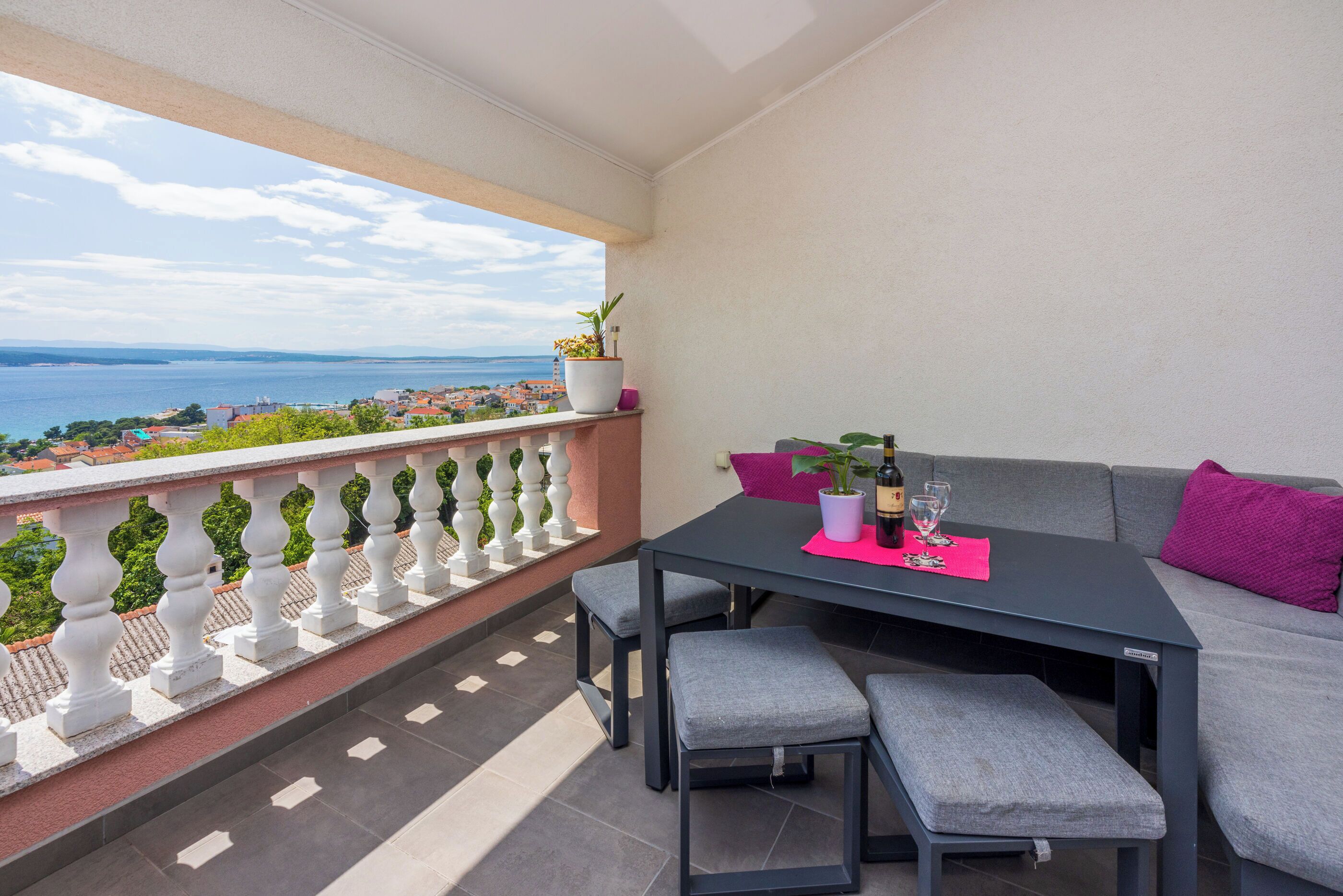 A balcony with a table and seating, overlooking a coastal view.