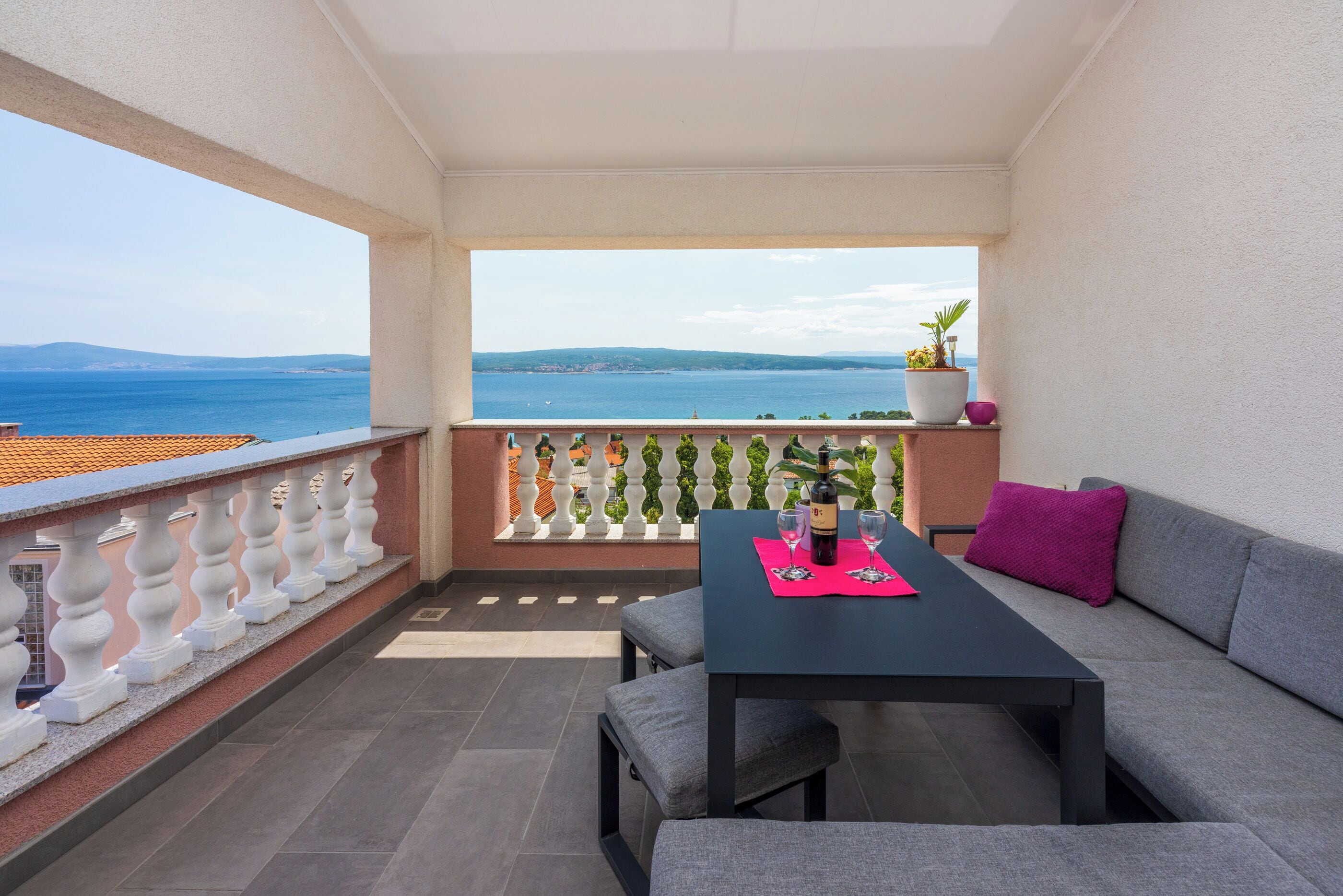 Ein Balkon mit Meerblick, ein Tisch mit einer Flasche und eine Couch mit Kissen.