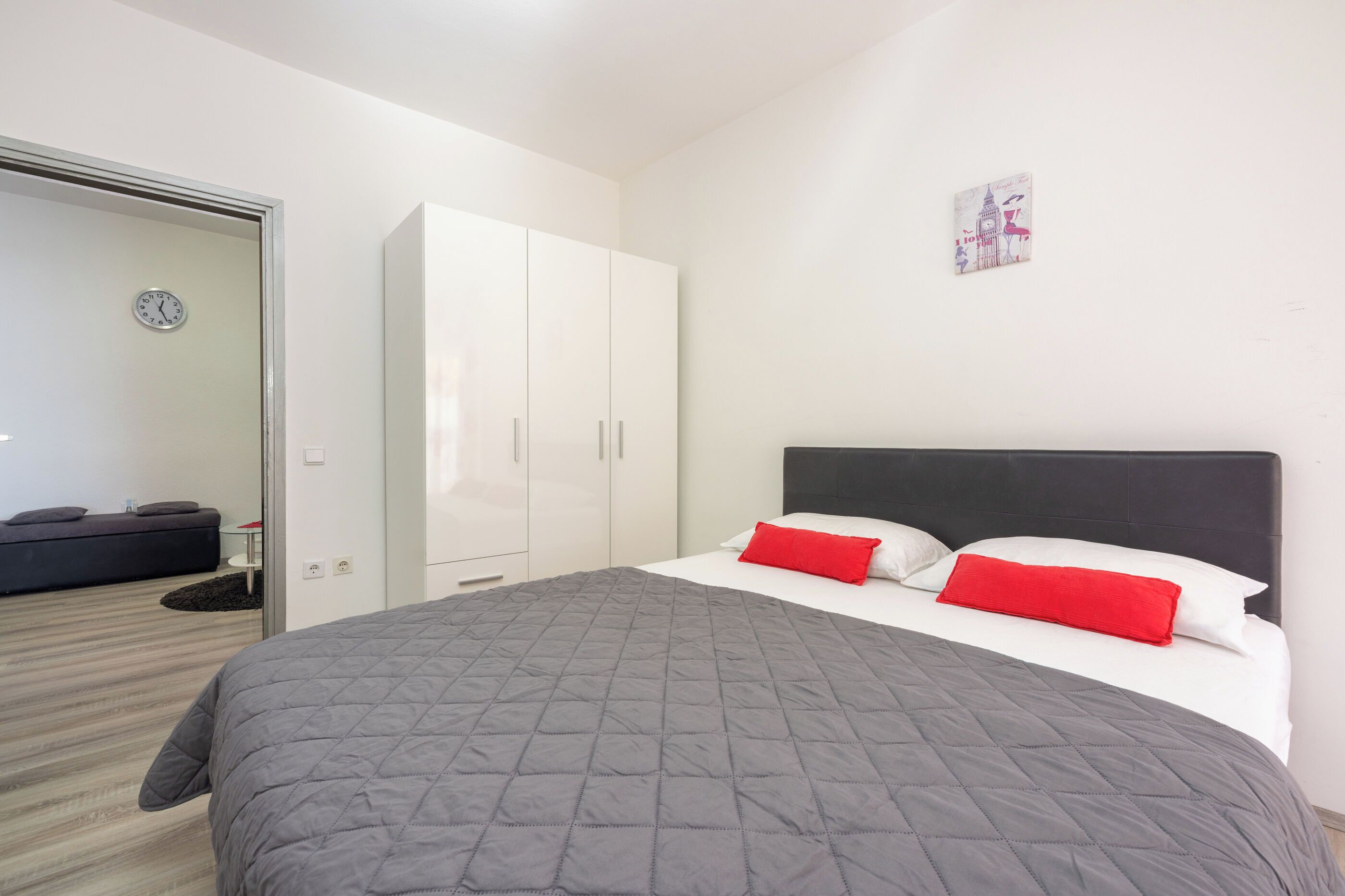 A neatly arranged bedroom with a bed, a wardrobe, and a clock on the wall.
