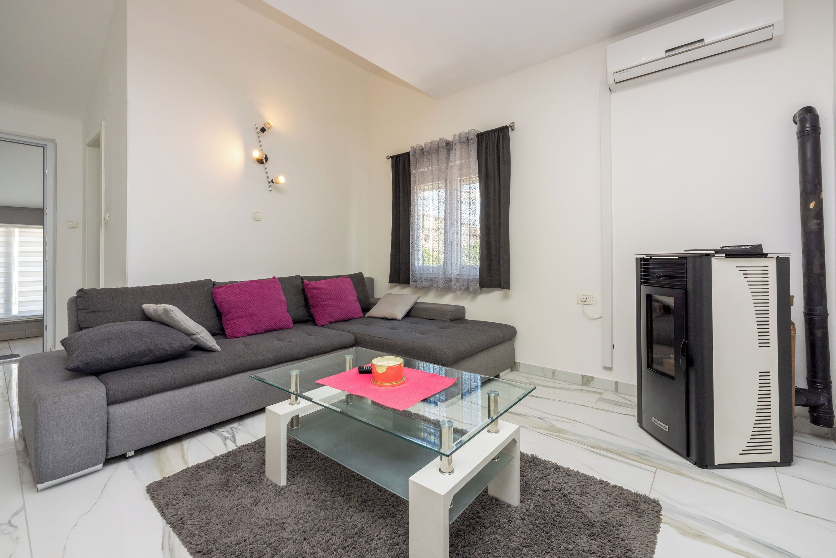 A modern living room with a grey sofa, a glass coffee table, and a black heater.