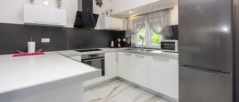 A modern kitchen with white cabinets, a stainless steel refrigerator, and a marble floor.