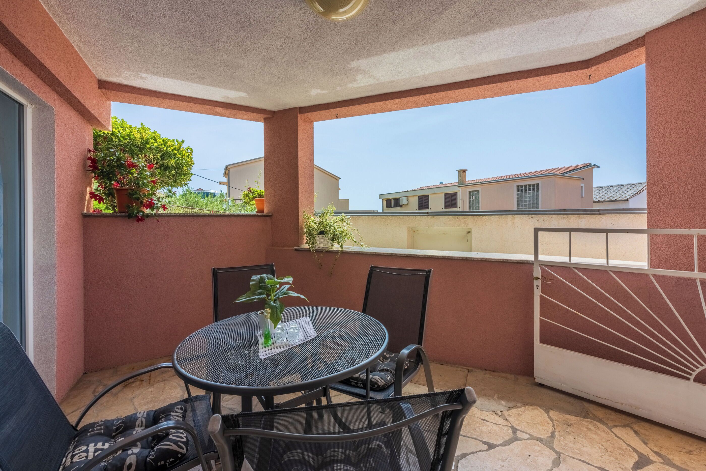 A balcony with a round table and chairs, potted plants, and a view of buildings.