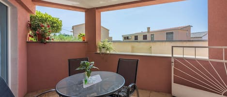 A balcony with a round table and chairs, potted plants, and a view of buildings.