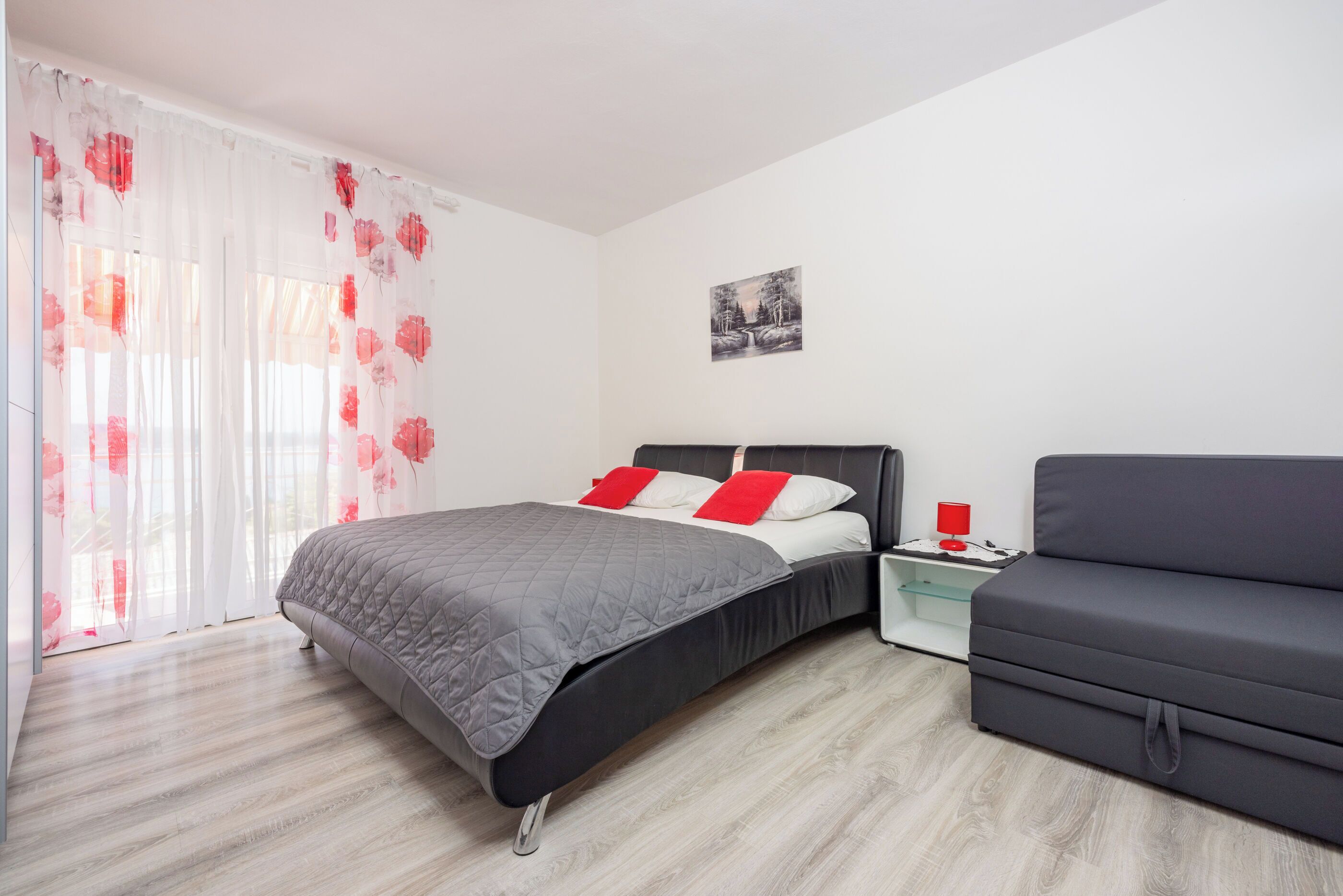 A bedroom with a bed, a nightstand, a sofa, and a window with curtains.