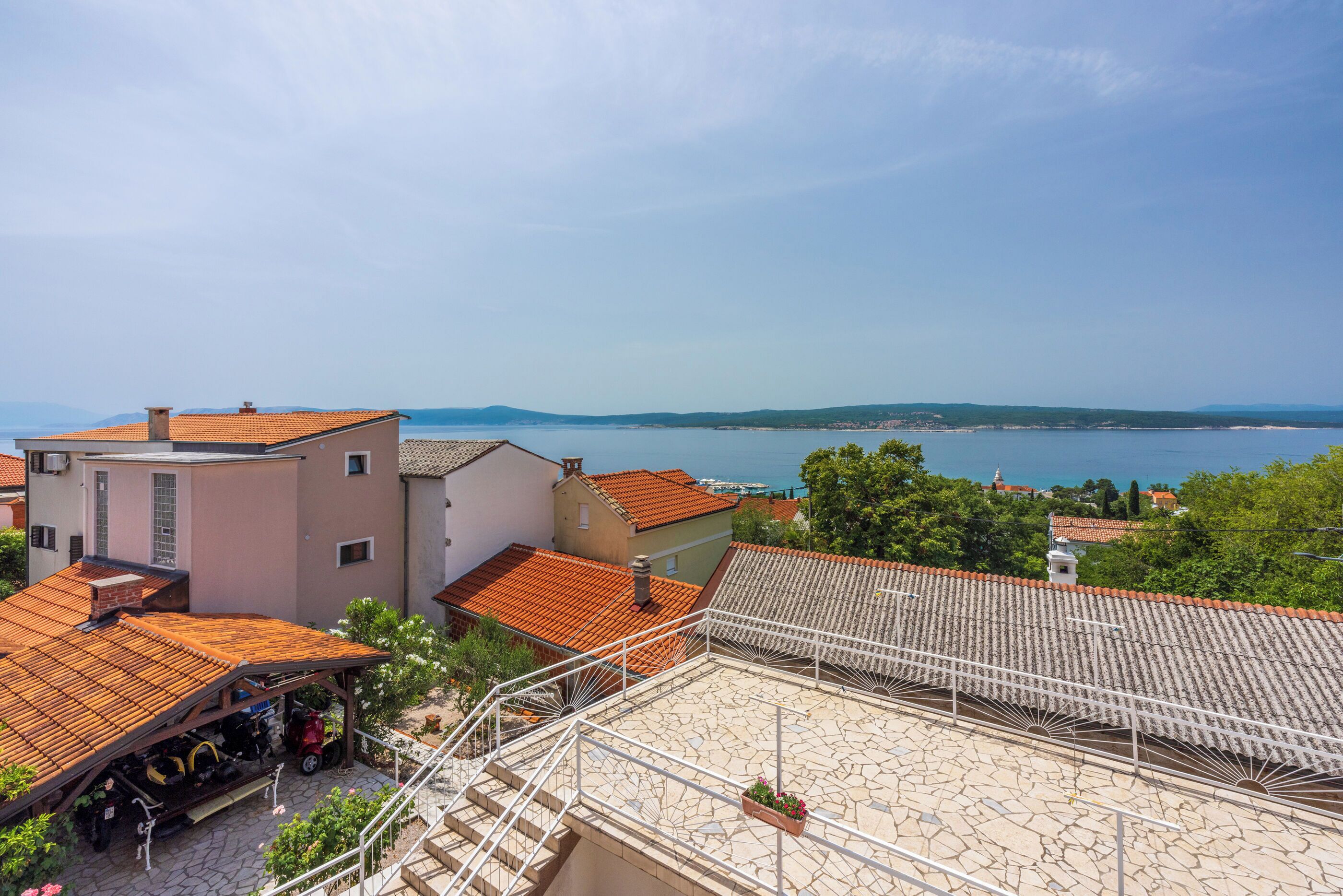 A residential area with terracotta-tiled roofs, a stone-paved courtyard, and a view of the sea.