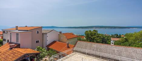 A residential area with terracotta-tiled roofs, a stone-paved courtyard, and a view of the sea.