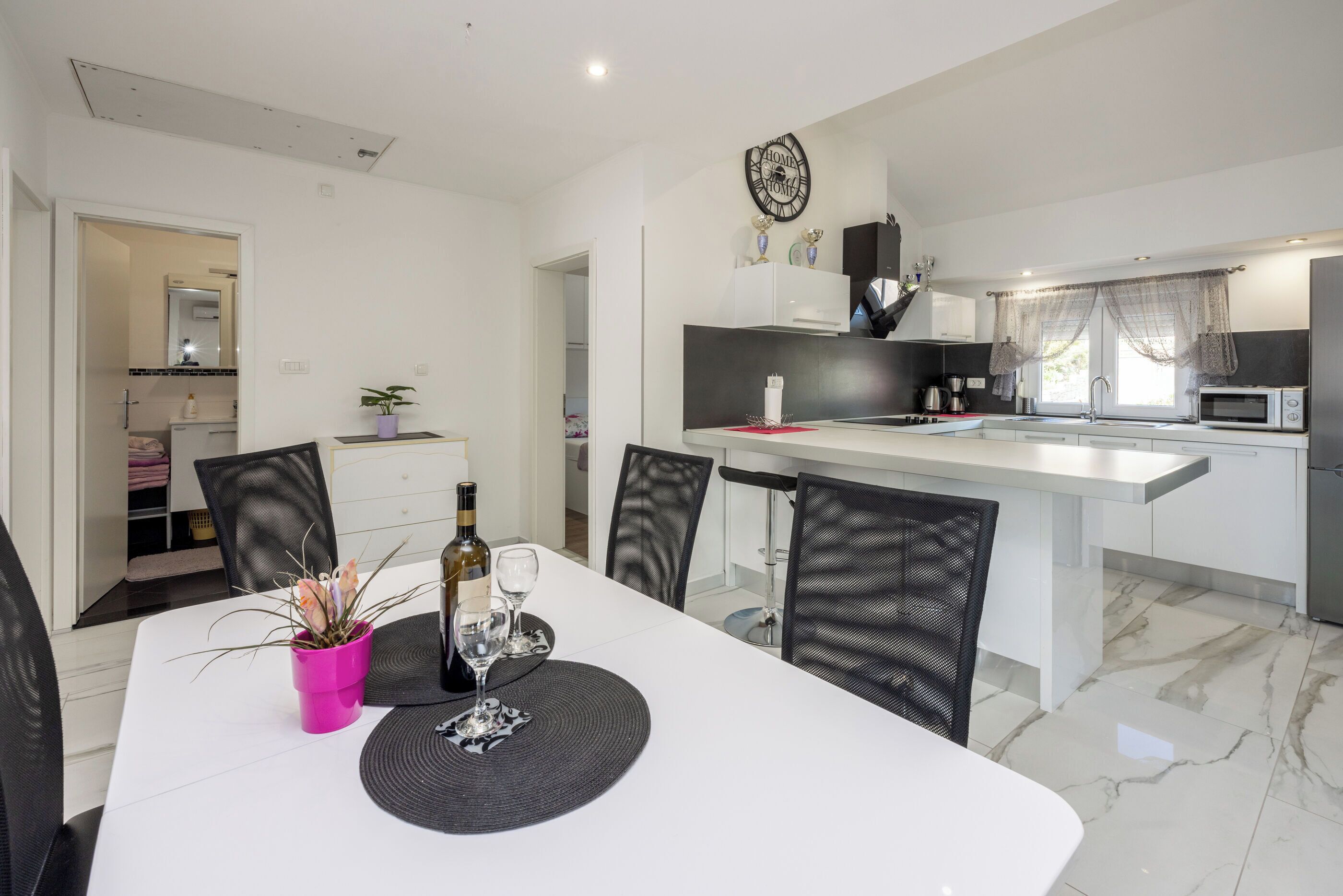 A modern kitchen with white cabinetry, a central island, and a dining area with a white table and chairs.