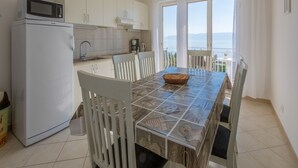 A kitchen with white cabinets, a microwave, and a dining table with chairs. - Apartment Duda (Novi Vinodolski)