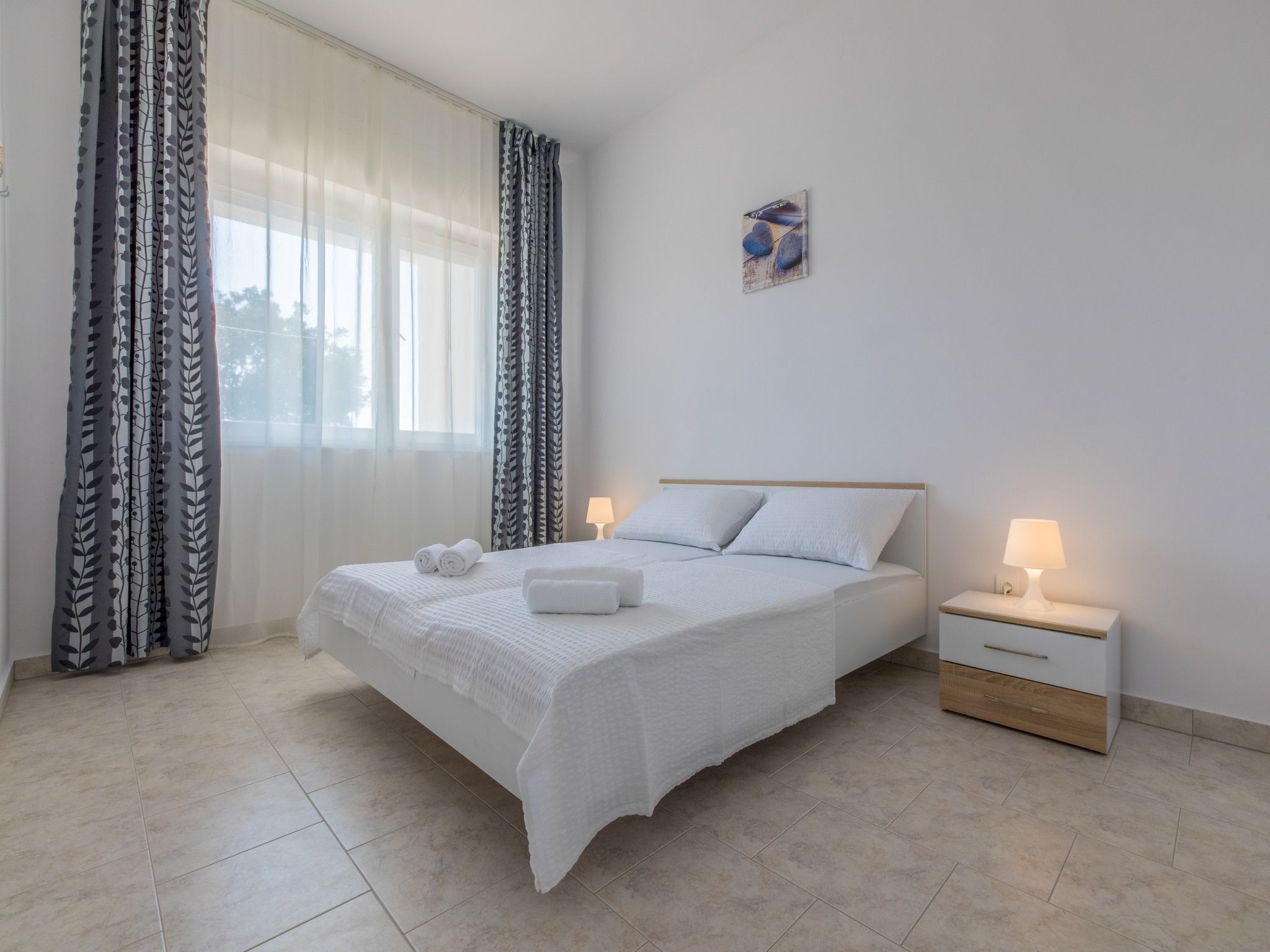 A neatly arranged bedroom with a bed, two bedside tables, and a window with curtains.