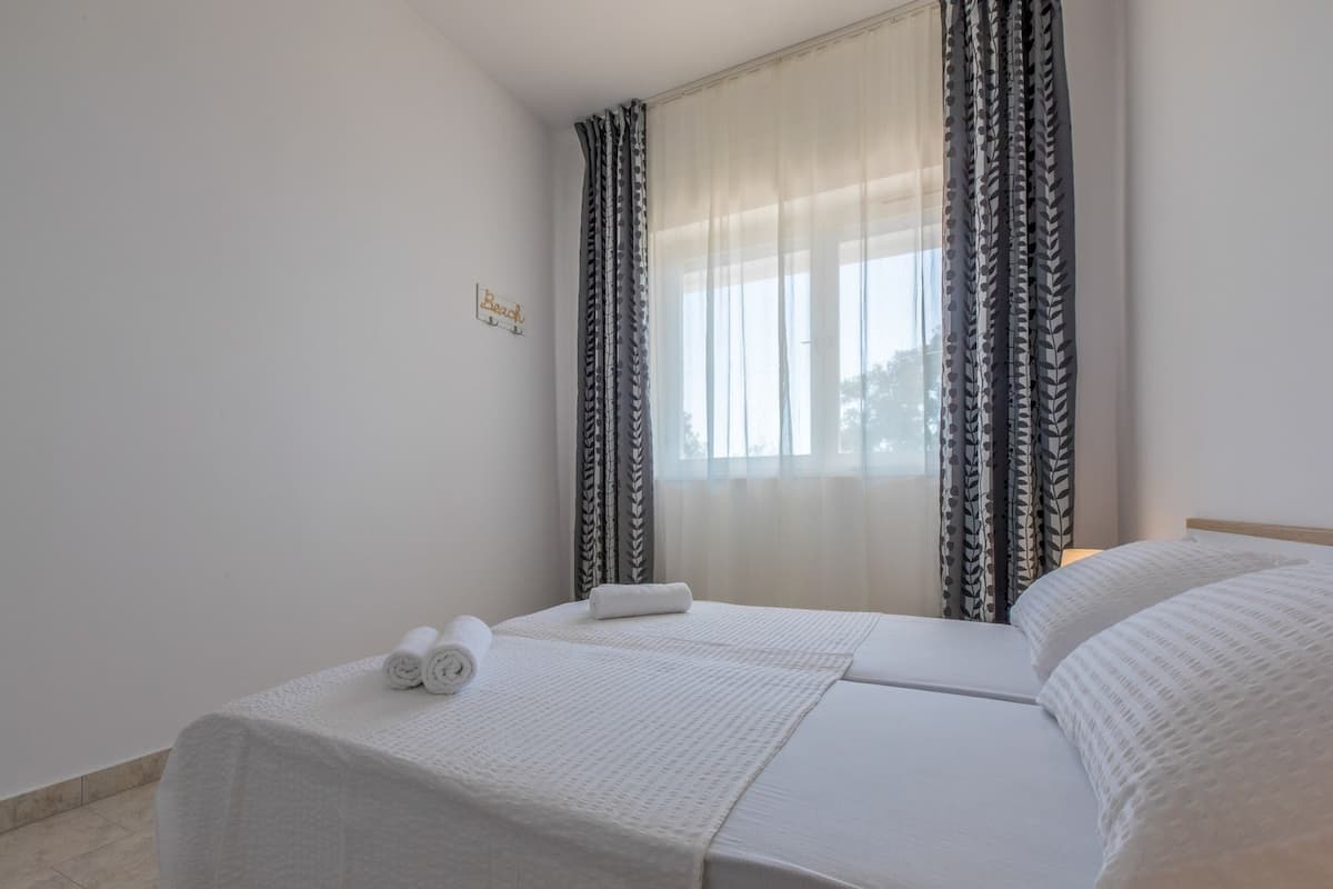 A neatly made double bed with white linens and a rolled towel on the side.