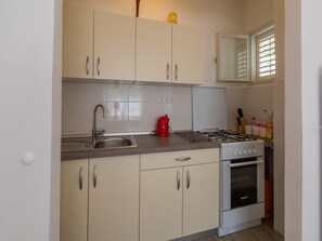 A compact kitchen with white cabinets, a stainless steel sink, a red kettle, a gas stove, and a built-in oven.