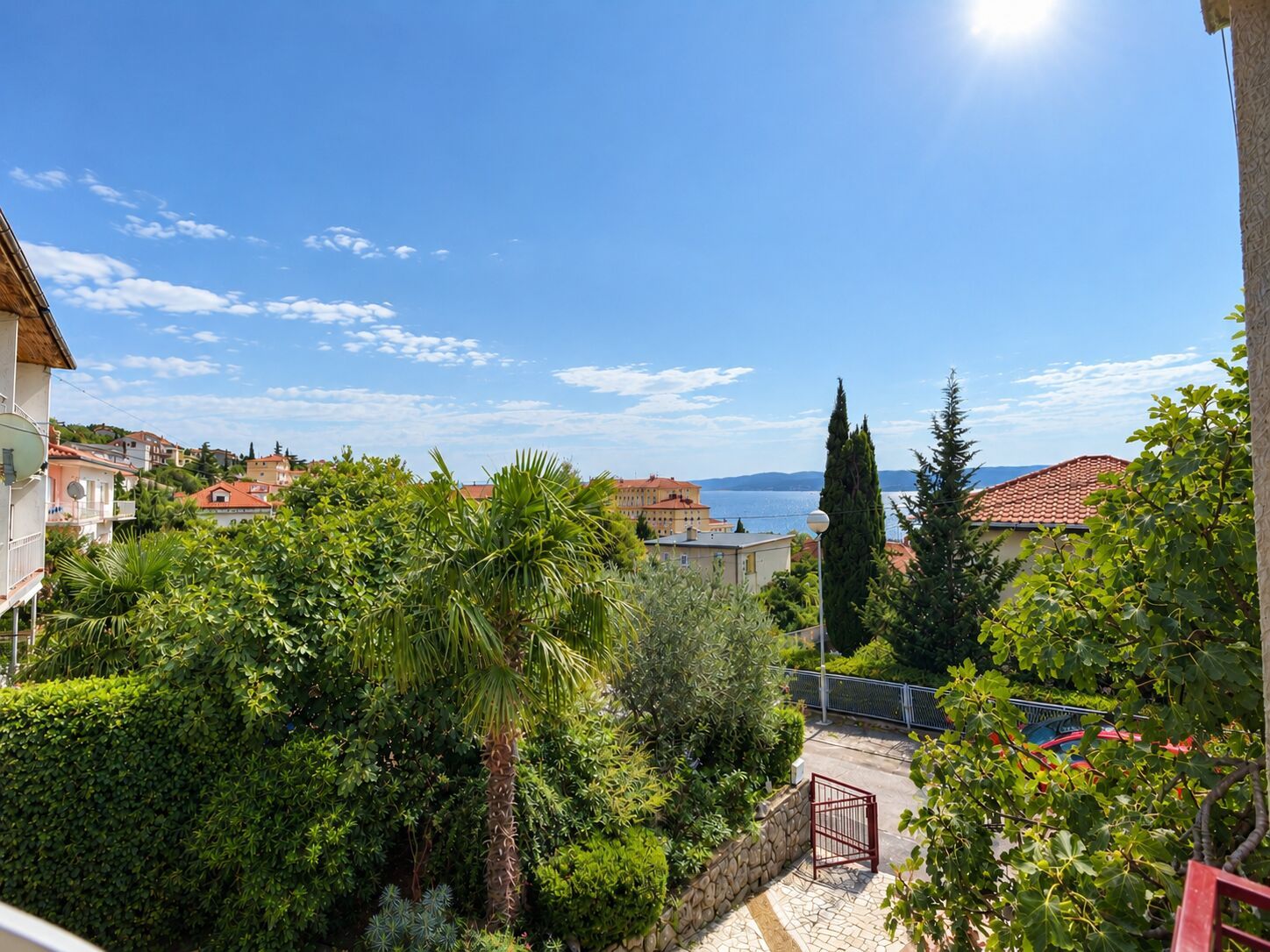 A residential area with a view of the sea, surrounded by lush greenery and buildings with red-tiled roofs.