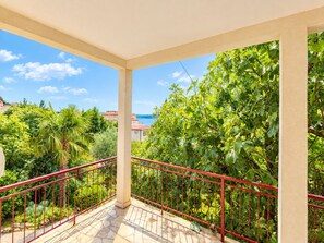 A balcony with a red railing, a tiled floor, and a view of greenery and a building across the street. - Apartment Mia (Crikvenica)