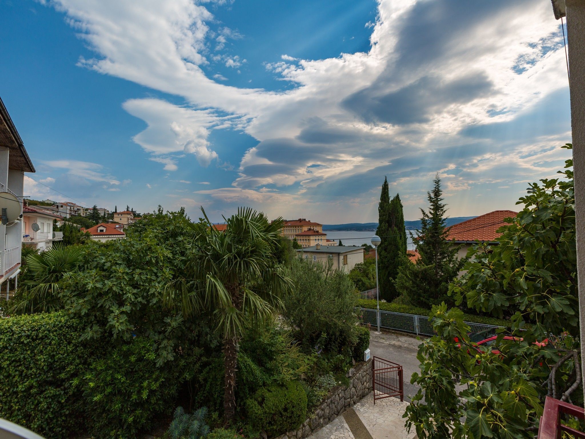 A residential area with a view of a body of water, surrounded by greenery and buildings with red-tiled roofs.