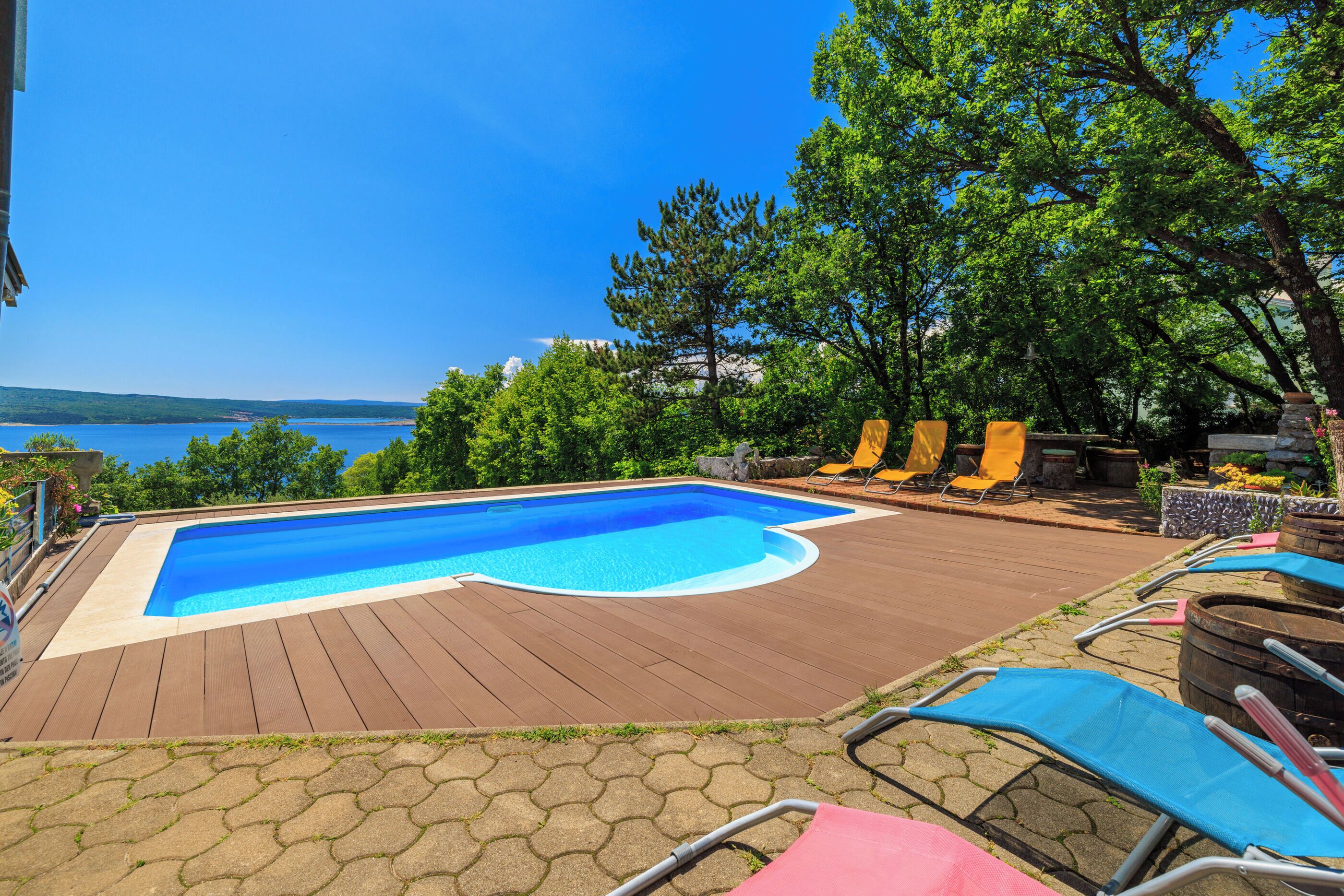 A swimming pool with a wooden deck, lounge chairs, and a view of the sea.