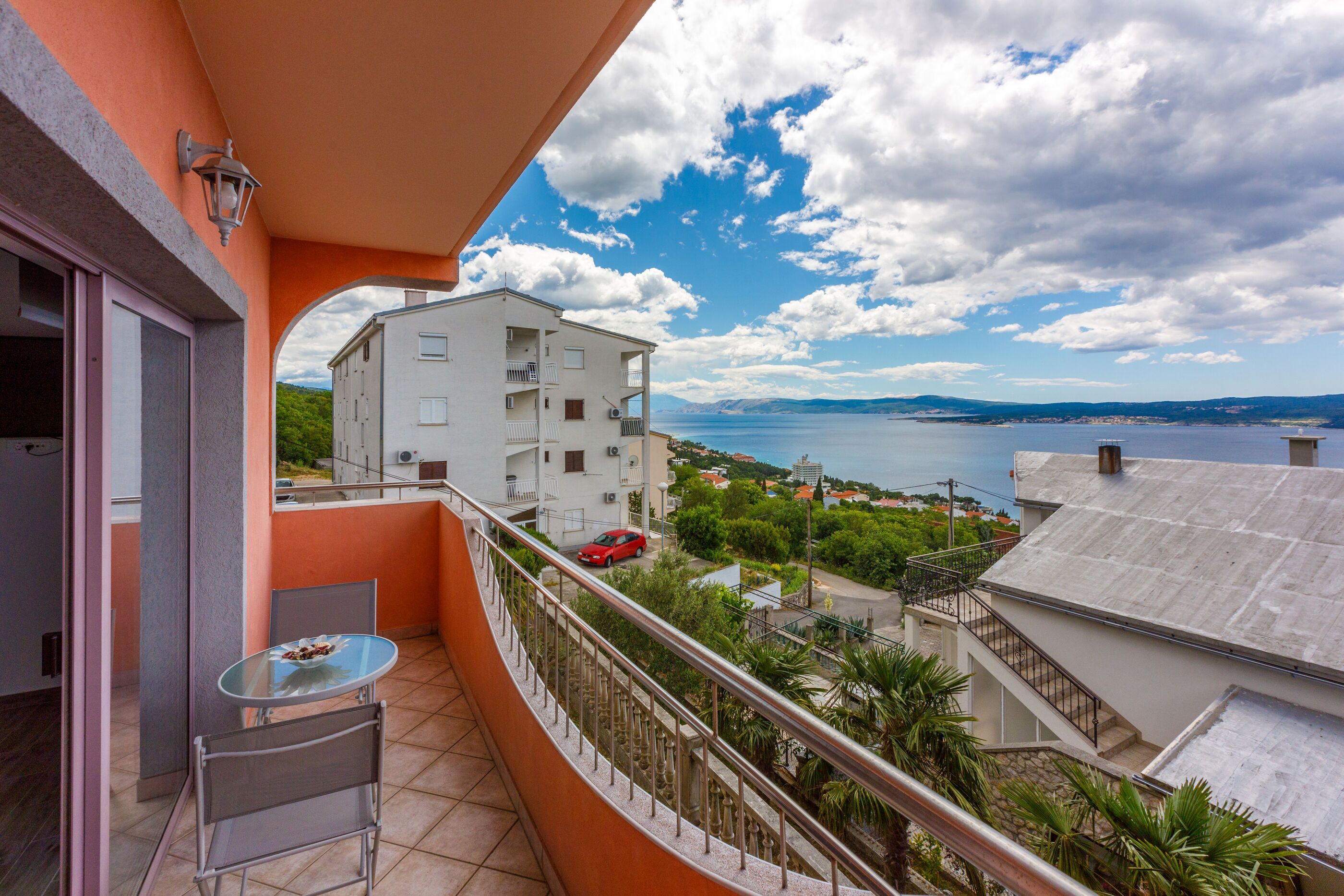 A balcony with a table and chairs, overlooking a body of water and buildings.