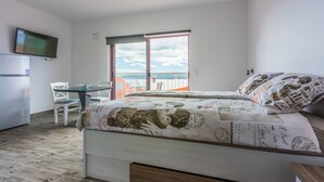 A bedroom with a bed, a TV, a desk, and a balcony with a view of the sea. - Apartments Djusi (Dramalj)