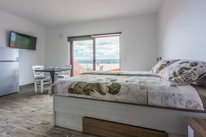 Et soveværelse med seng, fjernsyn, skrivebord og en balkon med havudsigt.