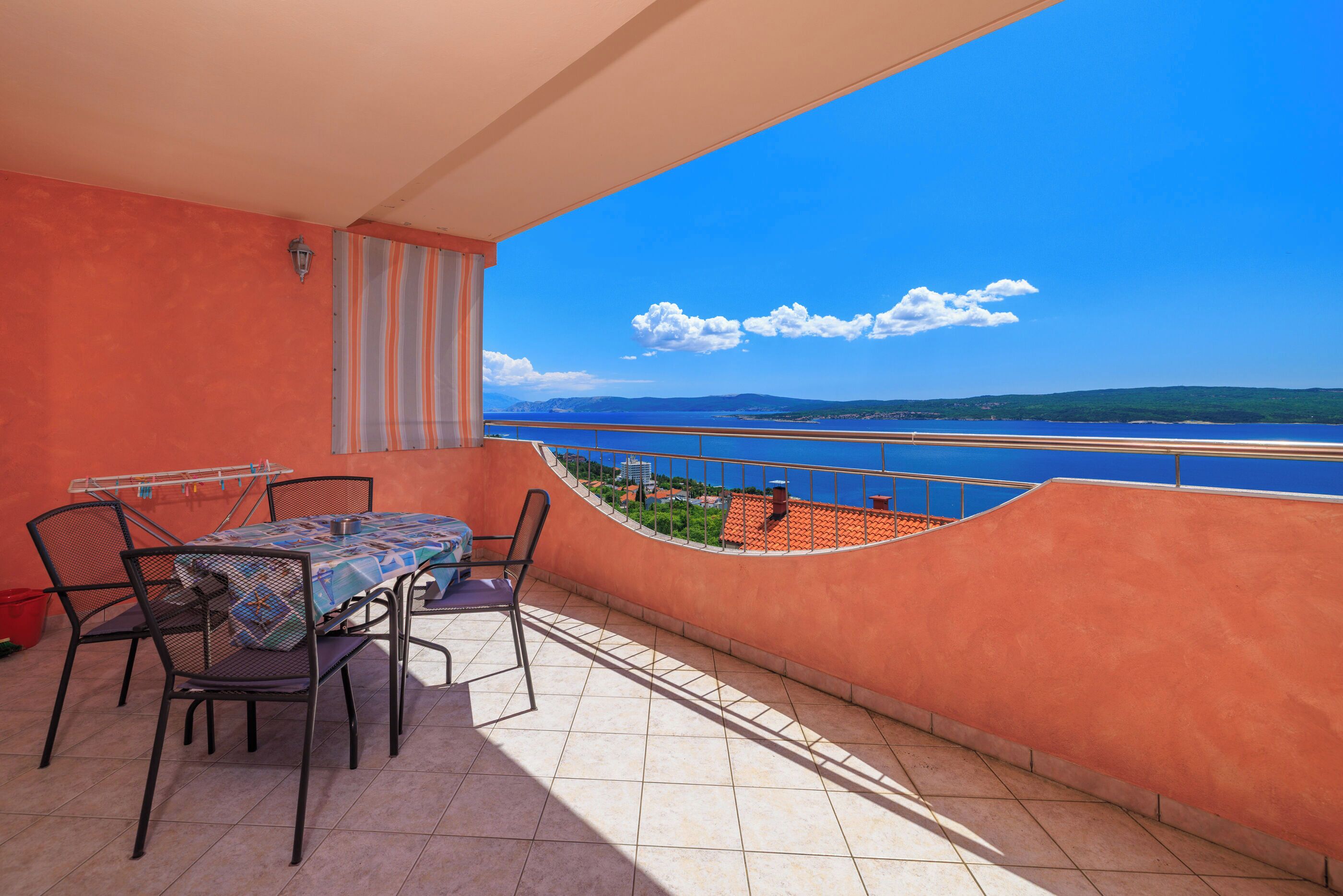 A balcony with a table and chairs, a view of the sea, and a tiled floor.