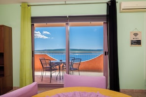 A room with a bed, a table, and chairs, a balcony with a view of the sea, and a sign indicating WiFi availability.